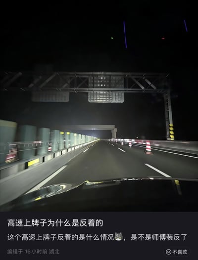 夜间高速公路上，从行驶车辆内拍摄的前方场景。画面中可见道路两侧的护栏、交通锥，以及上方的指示牌结构。图片底部配有文字：“高速上牌子为什么是反着的 这个高速上牌子反着的是什么情况😿，是不是师傅装反了”，表达了对高速指示牌方向的疑惑。