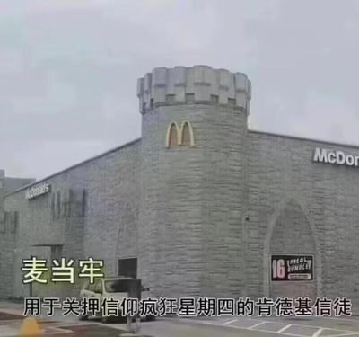 这是一张网友自制的搞笑梗图，将外观被修改为城堡监狱样式的麦当劳门店戏称为“麦当牢”，利用“麦当劳”与“麦当牢”的谐音梗，搭配文字说明“用于关押信仰疯狂星期四的肯德基信徒”，玩起了麦当劳与肯德基两大快餐品牌的对立梗。图中建筑为改造后的麦当劳门店，整体呈灰色城堡监狱外观，带有塔楼结构，塔楼处保留了麦当劳的金色拱门标识，墙面两侧有“McDONALDS”“McDon”的品牌字样，下方加注了玩梗的核心文字，结合肯德基“疯狂星期四”这一长期网络热梗，制造出荒诞又戏谑的搞笑效果。
