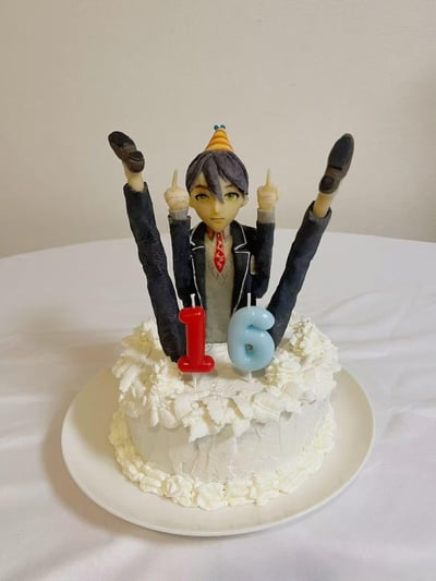 这是一款充满整活趣味的16岁生日蛋糕，蛋糕主体为白色奶油裱花造型，顶部插着红色数字“1”和蓝色数字“6”的生日蜡烛。蛋糕上的动漫男性角色被做成了搞笑的错位造型：原本的双腿被当作胳膊举在头顶，角色的双臂则做出竖中指的动作，头上戴着迷你生日礼帽，仿佛“坐”在奶油蛋糕中，整体造型搞怪新奇，没有双关、谐音梗或暗示内容。