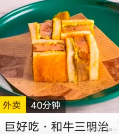 这是一张展示外卖送达状态的美食实拍图，标注了40分钟送达的和牛三明治被切成多块，放置在垫有仿报纸样式餐纸的绿色托盘上，面包外皮因外卖配送时间显得不再酥脆，内馅可见和牛肉类搭配酱料，图片下方配有“外卖 40分钟”和“巨好吃·和牛三明治”的文字，直观呈现了长时间配送后餐品的实际样子。