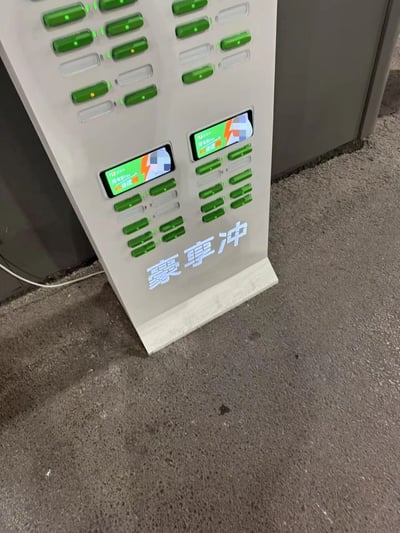 图片展示了一台共享充电设备，设备主体为银灰色，正面布满了绿色的充电接口，每个接口上方有指示灯。设备中部有两个小型显示屏，下方印有蓝色的“雾享冲”字样。整体看起来是公共场所常见的共享充电宝租借设备。