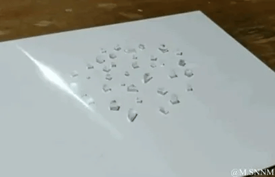 这是一段动态GIF内容，画面展示了白色平面纸张上散落的多块透明细碎晶体状物体，在无明显外力接触的情况下，这些碎块自行缓慢移动，呈现出逐渐聚集的趋势，画面右下角带有@MSNNM的水印标识。该内容无谐音梗、双关或暗示性内容。