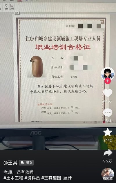 这是一张竖版的社交媒体内容拍屏截图，呈现的是抖音用户发布的搞笑整活图文。画面核心是显示在AOC品牌显示器上的《住房和城乡建设领域施工现场专业人员职业培训合格证》，证书编码、持证人姓名、身份证号均做了马赛克打码处理，明确标注岗位名称为资料员，载明持证人参加对应职业培训测试成绩合格，继续教育记录显示2021、2022两个年度均完成了32学时的继续教育。证书原本用于张贴个人证件照的位置，被替换成了一款将柴犬处理为圆柱香肠形态的搞笑表情包，柴犬侧脸朝左，神态平静略带无奈，形成错位笑点。截图完整保留了抖音移动端的交互界面：右侧栏依次显示发布者头像、加关注按钮、4.5万点赞、1341条评论、2442次收藏、9.2万次转发，底部标注发布者为@王其，内容类型为图文，配文为“老师，还有救吗”，附带多个相关话题标签，整体用戏谑的方式调侃建筑行业从业者的考证、证书相关经历，属于自嘲类的日常玩梗内容。