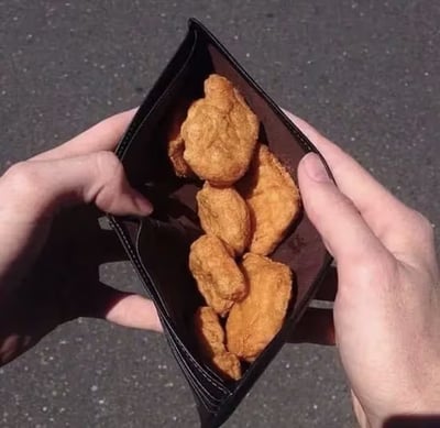 这是一张第一视角拍摄的趣味实拍图，画面中一双手翻开一个黑色的钱包，正常应该存放现金、银行卡的钱包内没有任何常规财物，反而装满了多块金黄色的油炸炸鸡块，背景是灰色的沥青路面。该图用反差感极强的内容玩梗，调侃对于创作者而言，炸鸡块是比金钱更珍贵的“财富”，以此回应“如何用一张图片证明你很有钱”的话题，充满幽默感。