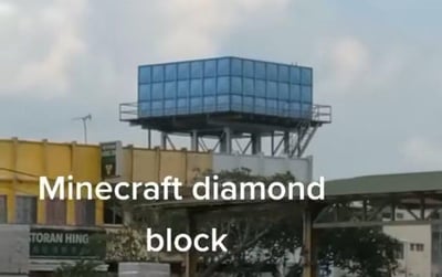 图片展示了一栋黄白相间的建筑，其顶部矗立着一个蓝色玻璃幕墙结构的水箱。画面下方叠加了白色文字“Minecraft diamond block”，将现实中的蓝色水箱幽默地比作《我的世界》（Minecraft）中的钻石方块，利用两者在颜色和方块形状上的高度相似性制造趣味联想。