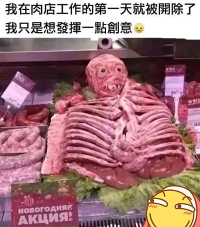 图片展示了肉店冷柜中的肉类陈列，生肉（可能为排骨等部位）被摆成类似骷髅的造型，头部有明显的眼睛和嘴巴轮廓。上方配有文字“我在肉店工作的第一天就被开除了 我只是想发挥一点创意 😐”，以幽默方式暗示员工因这种创意但可能令人不适的肉类摆放方式被解雇。左下角有红色标牌，上面有俄文“НОВОГОДНЯЯ АКЦИЯ!”（意为“新年促销！”），右下角有一个黄色调皮表情的小图标。整体营造出搞笑又无奈的氛围。