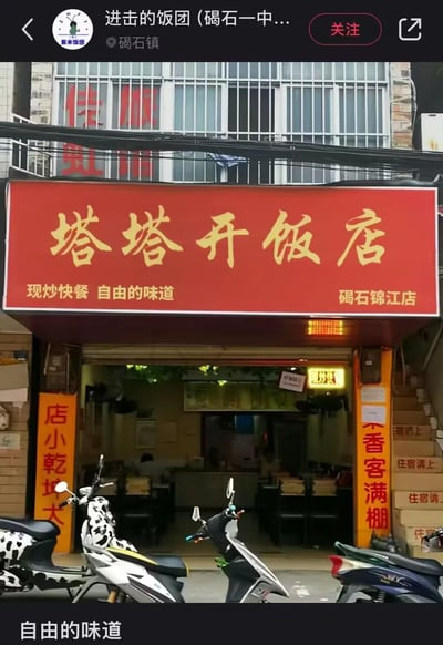 这是一张实拍的本地快餐店门店照片，店铺位于碣石镇，红色招牌搭配醒目的黄色大字店名“塔塔开饭店”，招牌下方标注“现炒快餐 自由的味道”与“碣石锦江店”，门店入口两侧有“店小乾坤大”“菜香客满棚”的标语，店前停放着几辆电动车，店内可见用餐区域。
谐音梗说明：“塔塔开”是日语“战斗”的中文空耳，和“开饭店”结合，让店名自带反差感，显得十分有趣接地气。
