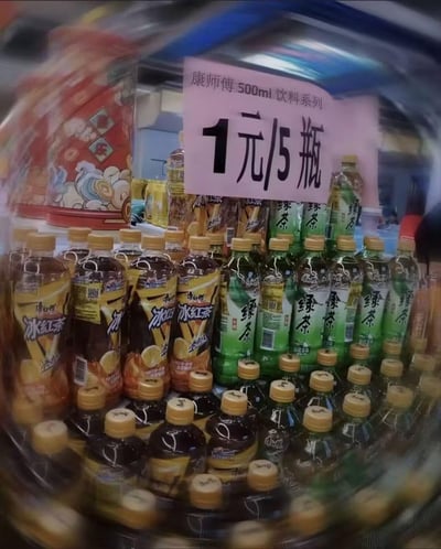 这是一张线下零售场景的实拍图，展示了冷藏柜中陈列的康师傅500ml装冰红茶与绿茶饮料，上方的粉色促销标牌醒目地标注着“康师傅500ml饮料系列 1元/5瓶”，柜内的冰红茶（棕色瓶身）和绿茶（绿色瓶身）整齐排列，超低价的促销信息极具吸引力，属于线下的特惠售卖活动，图中没有双关、谐音梗或暗示内容。