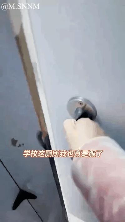 这是一张竖屏的原始实拍图，画面中一只手正在试图操作学校厕所的门把手，该门把手已经损坏，从门缝可以看到厕所内部的地面。图中加注了文字“学校这厕所我也真是服了”，直白地表达了拍摄者对学校厕所设施损坏、维护不到位的无奈与吐槽情绪，内容没有双关、谐音梗或暗示，是日常校园生活里的真实吐槽场景。