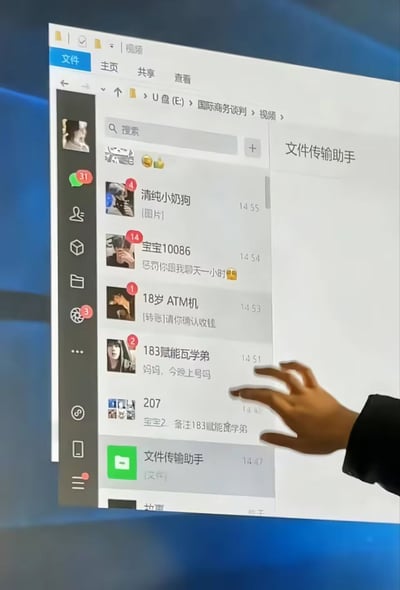 图片展示了一个电脑屏幕界面，左侧是文件资源管理器窗口，路径显示为“U盘 (E:) > 国际商务谈判 > 视频”；右侧是一个即时通讯应用界面，显示多个联系人列表。联系人名称充满幽默感，包括“清纯小奶狗”“宝宝10086”“18岁 ATM机”“183赋能学弟”等。其中“183赋能学弟”的最新消息为“妈妈，今晚上号吗”，一只手正指向该联系人，形成搞笑的反差效果——一本正经的文件夹路径与沙雕联系人名称及消息内容形成鲜明对比，充满生活调侃气息。
