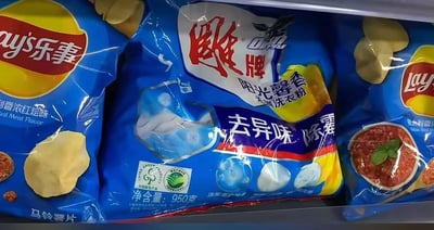 冰箱抽屉内整齐摆放着多包蓝色包装的乐事薯片，其中却意外混入一袋包装颜色相近的雕牌阳光馨香洗衣粉。洗衣粉包装上清晰印有“去异味 除霉”字样，与周围的薯片包装袋在视觉上形成强烈反差，营造出日常生活中因物品摆放错位产生的搞笑场景。