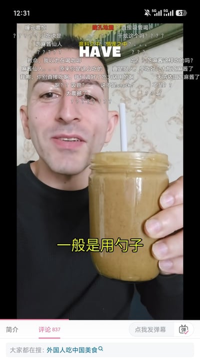 这是一张竖屏短视频截图，画面主体是一名穿黑色上衣的外籍男性，他手持一罐插着白色吸管的棕黄色芝麻酱对着镜头。画面上方覆盖了大量网友发送的弹幕，内容多为对男子用吸管直接喝芝麻酱的行为表示震惊，调侃他是“芝麻酱仙人”，还有网友提醒芝麻酱通常是调好了吃火锅用的，不能直接这么吃。画面中部有白色大写英文“HAVE”，下方配有黄色醒目字幕“一般是用勺子”。截图底部能看到短视频平台的界面，显示当前处于评论页，共有837条评论，搜索联想词为“外国人吃中国美食”。
