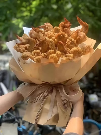 一张展示创意炸鸡虾花束的照片，将传统花束的形式与美食结合，用炸鸡块和炸虾代替鲜花，包裹在牛皮纸中并用丝带装饰。这种创意融合了浪漫与美食元素，适合作为给吃货朋友的特别礼物。