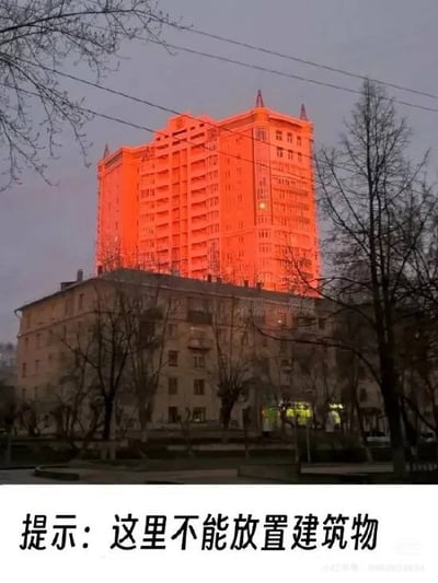 这张图片展示了一栋高楼建筑，奇怪地“叠”在另一栋楼的屋顶上，形成了视觉上的错位效果。配文“提示：这里不能放置建筑物”，让人联想到《我的世界》等沙盒游戏中建造时的报错提示，制造出幽默和超现实的效果。

图片利用了现实中的特殊角度造成的“建筑重叠”错位，成功营造了像游戏中物体不能叠加摆放的即视感。文案与画面巧妙结合，属于经典的现实版游戏梗图。

没有明显谐音梗或黄色暗示，但有强烈的游戏场景和调侃现实城市规划的双关意味。