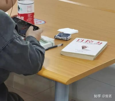 在类似自习室或图书馆的场景里，一名身穿深色外套的人正双手专注操作手机，而他面前的桌子上，却摆放着一本名为《自控力：斯坦福大学最受欢迎心理学课程》的书籍，桌上还有农夫山泉矿泉水、纸巾、笔等物品。画面形成强烈反差，讽刺了“明知要自控却无法做到”的普遍状态，十分搞笑又充满无奈。