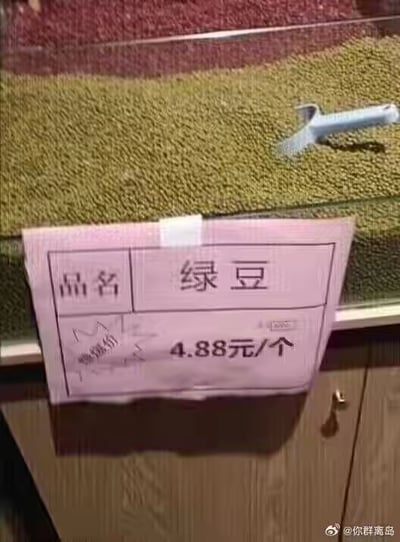 这是一张超市杂粮售卖区的实拍图，玻璃货柜中盛放着满满的绿豆，货柜外侧贴着一张粉色的手写价格标签。标签上清晰标注品名是“绿豆”，但计价单位却错误地写成了“个”，售价为4.88元/个。正常情况下，绿豆这类散装杂粮的计价单位应为“斤”或“500g”，以“个”为单位售卖绿豆显然不符合常理，这个乌龙的价格标签让原本普通的超市场景变得十分滑稽搞笑。