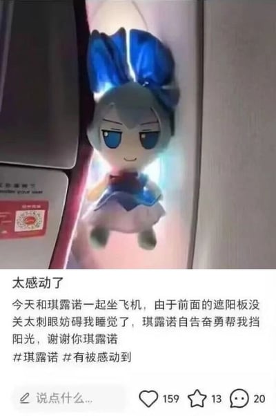 这张图片是在飞机上拍摄的，一只穿着蓝色裙子的玩偶（琪露诺）被夹在飞机窗和盖板之间，仿佛在帮拍摄者遮住阳光。配文用拟人化方式表达了对玩偶“自告奋勇”帮助挡阳光的感谢。整体氛围温馨搞笑，适合用来表达‘朋友为我分担’或‘可爱同伴的暖心陪伴’等情感。