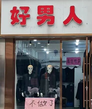 这是一张原始拍摄的静态竖图，展示了一家名为“好男人”的线下男装实体店铺。店铺招牌使用醒目的红色大字书写“好男人”，十分显眼。店铺玻璃门内可以看到悬挂陈列的男装服饰，橱窗内有两个穿着深色上衣的人体模特，模特面无表情，保持静止站立的姿态用于展示服装。玻璃门上贴着两张粉色手写纸张的告示，右上角的纸张写着“清仓甩卖”，门下方的纸张写着“不做了”，清晰地传达出这家男装店铺即将停止营业，正在进行结业清仓的信息。