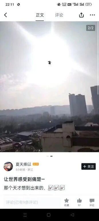 这是一张社交媒体平台的截图，用户“夏天乘以”发布了一张城市户外拍摄的照片，照片中明亮的太阳附近有一个黑色的高空物体，看起来像是无人机，背景是城市的高楼建筑群和地面停车场。配文“让世界感受到痛楚—那个天才想到出来的，😇😇😇”，表达了对这个高空物体的吐槽，推测是不满该物体在强光环境下飞行带来的困扰。