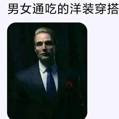 图片上方有文字“男女通吃的洋装穿搭”，下方是一位穿着深蓝色西装、白色衬衫、蓝色领带并佩戴红色口袋巾的男性。他头发呈浅色，表情严肃，背景为深色。这张图通过标题与内容的反差制造幽默效果，标题声称是“男女通吃”的穿搭，但展示的却是非常传统的男性西装形象。