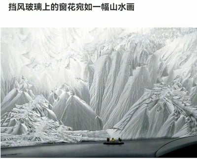 图片展示了汽车挡风玻璃上的窗花景象，冰霜凝结形成的纹理层层叠叠，宛如一幅意境悠远的中国山水画。画面下方可见汽车仪表盘的部分区域，上面放置着一个小型装饰物。图片上方配有文字'挡风玻璃上的窗花宛如一幅山水画'，点明了窗花与传统山水画的相似之处，展现了大自然的鬼斧神工。