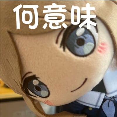 这是一张文字加注的表情包，主体是《BanG Dream! It's MyGO!!!!!》中长崎爽世的周边毛绒玩偶，玩偶有着浅棕色头发与蓝灰色眼睛，面带温和的微笑。图的上方用醒目的白色大字覆盖了日语“何意味”（意为“什么意思”），用来传递疑惑、不解的情绪，适合在遇到难以理解的事物或场景时使用，风格软萌又带着困惑感。