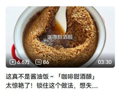图片展示了一锅咖啡甜酒酿，棕褐色的米粒在锅中呈现，表面有光泽，中间插着一把白色勺子。由于颜色与酱油饭相似，图片下方文字特意说明“这真不是酱油饭…「咖啡甜酒酿」太惊艳了！锁住这个做法，想失…”，并显示该内容有6.6万次观看、86条评论，视频时长03:30，整体是一则推荐创意美食做法的视频截图。