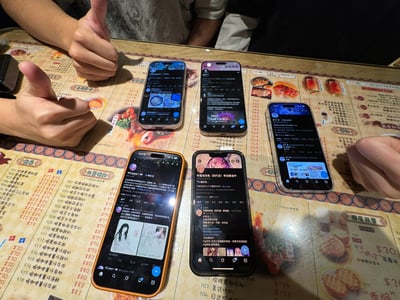 图片展示了尖沙咀红茶餐厅内的聚餐场景，桌面上铺着印有菜品名称和价格的菜单（如“201 招牌奶茶”“焗猪扒饭”等），五只智能手机屏幕亮着并显示不同内容，其中一只手机屏幕可见“早露泡泡兔（四代目）寻回推油中”字样。周围有多只手竖起拇指点赞，整体氛围轻松，呈现出聚餐时众人围绕手机互动的日常画面。
