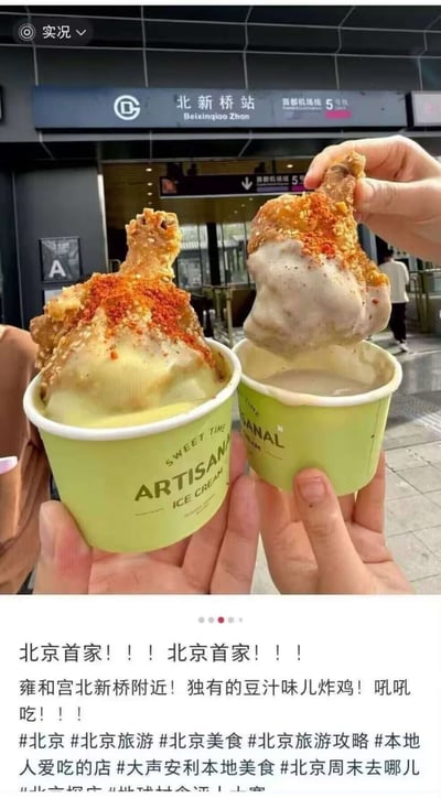 这张图是网友分享的美食种草内容，前景可见三只真人的手，两只手分别握持印有“ARTISANAL ICE CREAM”字样的浅绿色冰淇淋纸杯，杯中分别盛放奶黄色、浅棕色的冰淇淋，每杯冰淇淋上都放置了一根表面撒有辣椒粉的炸鸡腿，第三只手正拿起蘸有浅棕色冰淇淋的炸鸡腿进行展示。背景为北京地铁北新桥站的入口区域，清晰可见带有“北新桥站 Beixinqiao Zhan”以及5号线标识的站名牌。图片下方配文宣传该美食是北京首家位于雍和宫北新桥附近的店铺推出的独有豆汁风味炸鸡，夸赞其口味好，还附带了多个与北京旅游、北京美食相关的话题标签，属于本地美食安利内容。