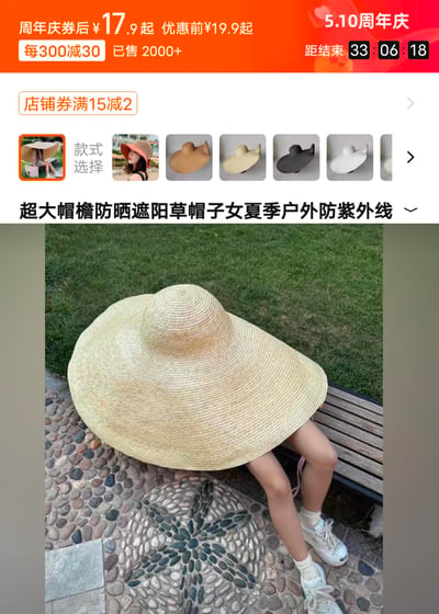 这是一张电商平台的商品详情页截图，展示了一款主打夏季户外防紫外线的超大帽檐防晒草帽。页面显示正值5.10周年庆活动，该草帽券后价17.9元起，优惠前19.9元起，支持每300减30、满15减2的满减优惠，已售出2000+件，活动倒计时33小时6分18秒。图中模特坐在户外长椅上，被这款几乎能遮住上半身的超大草帽挡住头部和躯干，直观展现产品超强的遮阳范围，同时页面还提供了多款不同款式、颜色的草帽供消费者选择。