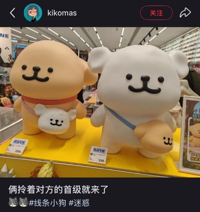 图片展示了玩具店货架上的两个可爱毛绒玩具：一只黄色的线条小狗和一只白色的小熊。线条小狗脖子系着红色项圈，怀里抱着一个迷你白色小熊玩偶；白色小熊脖子系着蓝色项圈，怀里则抱着一个迷你黄色线条小狗玩偶。两者都有着圆润的脑袋和微笑的表情，看起来十分治愈。然而图片下方的配文“俩拎着对方的首级就来了”却用夸张的“首级”一词形容它们抱着对方玩偶的动作，形成可爱外表与搞笑文案的强烈反差，让人忍俊不禁。