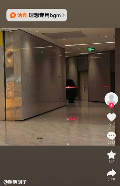 这是一张竖版的短视频平台内容截图，拍摄场景为写字楼8楼的公共走廊，走廊墙面和地面都使用了高反光的大理石材质，走廊尽头区域停着一辆理想汽车，地面的反光刚好完整呈现了车辆红色尾灯及下半部分车身的倒影，和远处的墙体结合后形成了视觉错位，看起来仿佛理想汽车直接开进了写字楼走廊内部。图片顶部带有平台话题标签“理想专用bgm”，左下角标注内容发布者ID为@明明明子，图片右侧是短视频平台标准交互按钮，分别显示点赞数9786、评论数2178、收藏数340、转发数2.2万。