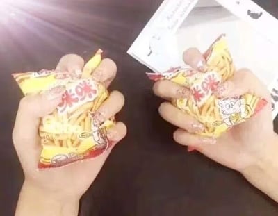 这是一张利用视觉错位拍摄的趣味照片，画面中一只手握着一包咪咪虾条，看起来像是长了六根手指，但实际上是另一只手的两根手指巧妙地放在这只手的旁边，制造出了“六指手”的视觉错觉，创意十足，充满趣味性。