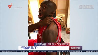 这是广东卫视《直播全球》节目的新闻截图，画面中一名中超黑人外援因没涂防晒霜被晒黑，露出夸张惊讶的表情，右手扯着球衣肩部展示被晒黑的皮肤，配文“没涂防晒霜 中超黑人外援被晒黑”和“我被晒黑了”，利用黑人被晒黑的强烈反差制造搞笑效果，成为有趣的防晒趣事新闻。
