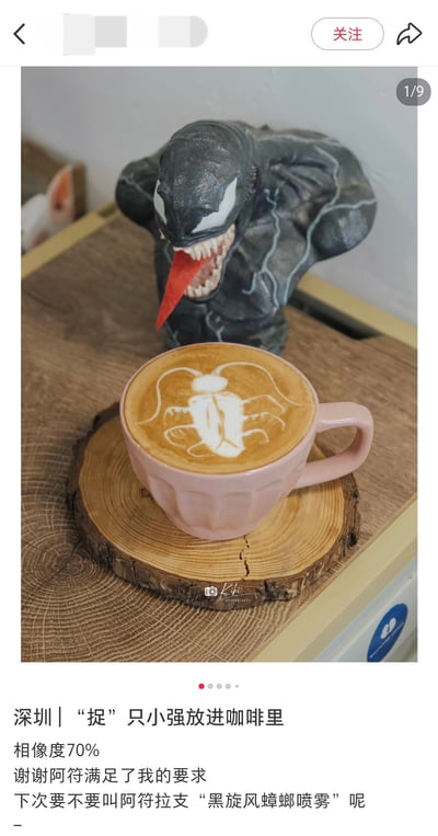 图片展示了一杯放在木质杯垫上的粉色咖啡杯，杯中拉花呈现出类似蟑螂的形象，呼应了2024年末爆红的‘广式双马尾’梗（将蟑螂超长触角比作双马尾）。杯后有一个毒液手办，其狰狞的表情与可爱的拉花形成反差萌。下方配文提到‘深圳 | 捉只小强放进咖啡里’，调侃拉花与蟑螂的相似度达70%，并幽默提议将咖啡师称为‘黑旋风蟑螂喷雾’，充满网感与地域趣味。