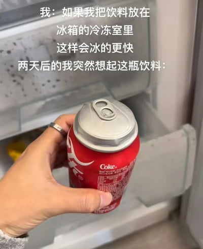 这是一张记录生活小失误的实拍图片，图中上方的文字描述了事件的前后过程：一开始“我”打算把饮料放进冰箱冷冻室让它快速变冰，结果过了两天才想起这瓶可口可乐。画面中一只戴着银色戒指的手拿着一罐红色的可口可乐，可乐罐的顶部因为内部液体结冰体积膨胀而严重凸起变形，背景是打开的冰箱冷冻室内部，能看到冷冻室的隔层和内壁，直观展示了液体结冰膨胀导致容器变形的物理现象，充满了生活中的小趣味和小尴尬。