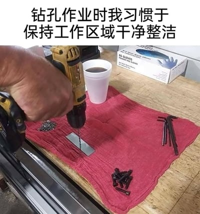 这是一张带有反讽意味的搞笑实拍图，画面上方配文“钻孔作业时我习惯于保持工作区域干净整洁”，但实际场景中，作业者直接在铺有红色毛巾的木质桌面上进行钻孔操作，毛巾上还随意摆放着装有液体的白色咖啡杯、螺丝、内六角扳手、金属环等物品，这种所谓的“整洁”完全是自我调侃，正常钻孔作业应在专业工作台或合适的夹具上进行，这样的操作不仅无法真正保持整洁，还可能损坏桌面与毛巾，用反差感制造出搞笑效果，调侃那些看似讲究实际操作随意的工作习惯。
