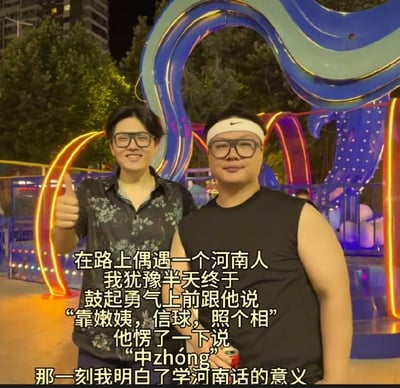 这是一张实拍加文字叠加的搞笑梗图，拍摄场景为夜晚的户外街头，背景可见带有蓝、黄等彩色灯光的游乐设施、行道树与居民楼。画面中有两名戴黑框眼镜的男子，左侧男子穿黑底带灰色花纹的短袖衬衫，面带笑意，右手抬起竖大拇指；右侧男子穿黑色无袖上衣，头戴印有耐克标志的白色发带，手持罐装饮品，表情平和。图中叠加的文字玩了谐音梗，将河南方言里的不雅脏话谐音伪装成“可以姨，幸会，照个相”的礼貌表述，讲述主人公用这段谐音话找偶遇的河南人请求合影，对方答应后主人公调侃自己终于懂了学河南话的意义，借谐音歧义制造笑点。