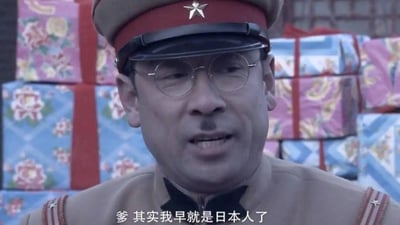 这是一张抗日题材影视剧的截图，画面中的男子头戴带有五星标识的日军风格军帽，戴着圆框眼镜，身着军装，正对着对话对象（台词中的“爹”）一本正经地说出“爹 其实我早就是日本人了”的台词。该剧情逻辑荒诞，人物身份与台词形成离谱反差，成为网友用来吐槽抗日神剧离谱设定的玩梗素材，图中无谐音梗、双关或暗示内容。