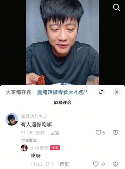 图片上半部分为一名身穿深色运动T恤的男子，手持一块红色食物（疑似魔鬼辣椒零食），表情略显忍耐，似乎正在进行辣味挑战。下半部分是社交媒体平台的评论区界面，顶部显示“大家都在搜：魔鬼辣椒零食大礼包”，下方有52条评论。其中用户“深藏功与名”于11月25日从吉林评论“有人逼你吃嘛”，获5赞；作者“小伙造奥”从辽宁回复“吃呀”，获10赞。整体呈现了一段真实的辣味零食试吃视频截图及互动评论场景。