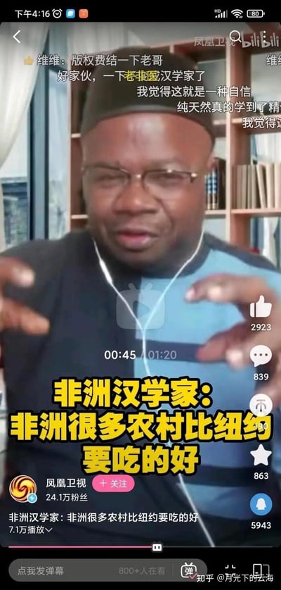 这是一张bilibili平台上凤凰卫视发布的访谈视频截图，画面中的非洲汉学家戴着耳机，双手做出手势，正在阐述“非洲很多农村比纽约要吃的好”的观点。视频上方有网友的弹幕评论，比如“版权费结一下老哥”“我觉得这就是一种自信”等，该视频播放量7.1万，截图时显示有800+人正在观看，画面右下角还有知乎用户的水印，整体是一个引发网友讨论的跨地域饮食观点的访谈片段。