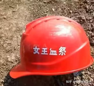 这是一张经过P图改编的照片，画面主体是一顶放置在泥土地面上的红色工地安全帽，安全帽表面被添加了白色的“女王血祭”字样。原本用于工地安全防护的严肃安全帽，搭配上带有猎奇感的文字，形成了强烈的反差感，以此制造出搞笑、猎奇的玩梗效果。