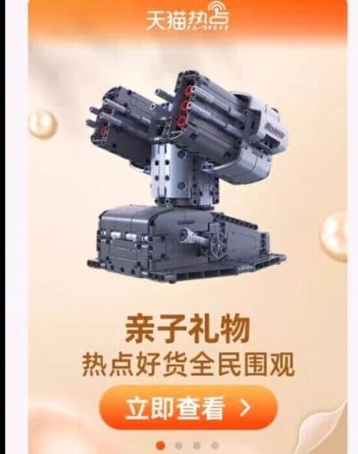 这是一张竖屏手机格式的静态商品推广图，属于顶配底文图类型。图中核心展示的是一款由黑、灰色积木拼装而成的多管炮台模型，模型结构精细，拥有两组多管发射装置，底座为履带式设计，充满机械感与科技感。图的顶部有“天猫热点”的水印文字，下方配有“亲子礼物 热点好货全民围观”的宣传文案，最下方设置了橙色的“立即查看”按钮，用于引导用户点击了解商品详情，整体内容是为这款积木模型做电商推广，将其定位为适合亲子的礼物。
