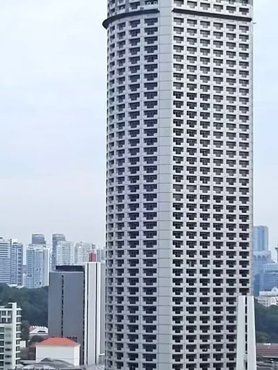 这是一张城市景观实拍静态图，画面主体是一栋外观造型独特的超高层摩天大楼，楼体外立面为浅灰色，布满了整齐排列的深色凹入式方形窗户，密集规整的排布使整栋楼的视觉效果格外酷似竖立起来的电脑键盘。大楼周边环绕着多座高低不同的其他城市建筑，远处背景为浅淡的灰蓝色天空，整体是典型的城市核心区建筑景观。