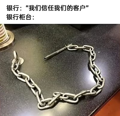 这是一张吐槽银行言行不一的幽默梗图，图片上方配有文字“银行：‘我们信任我们的客户’”，下方则展示了银行柜台的真实场景：一支签字笔被粗重的铁链牢牢拴在台面上。这种嘴上宣称信任客户，实际却通过铁链防止笔被带走的行为形成了强烈的反差，用夸张的方式讽刺了现实中这类“说一套做一套”的现象，以生活化的细节引发观众共鸣，充满趣味吐槽的意味。