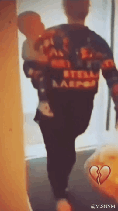 这是一张视觉错位的动态图，画面中一位大人将小孩扛在肩头行走，由于拍摄角度的巧合，让画面产生了奇妙的视觉错觉：看起来像是大人的身体上长着小孩的脑袋，小孩的身体则和大人的脑袋重合，形成了怪异的“拼接人”效果。右下角的破碎爱心表情符号，为这个搞笑的场景增添了一丝无奈感，图中没有双关、谐音梗或暗示内容。