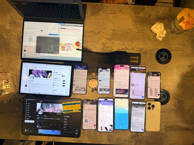 一张俯拍的办公桌场景，桌面上整齐摆放着多台数码设备：上方是一台打开的笔记本电脑，屏幕显示着包含代码和动漫人物的界面；中间是一台平板电脑，屏幕展示着带有动漫图片的网页；下方则排列着8部智能手机，每部手机屏幕都显示着不同的应用界面（如社交媒体、聊天软件等）。桌面上还散落着无线充电器、折叠的纸巾、带有图案的杯子和一些小饰品，整体呈现出一个充满科技感的个人工作或娱乐空间。