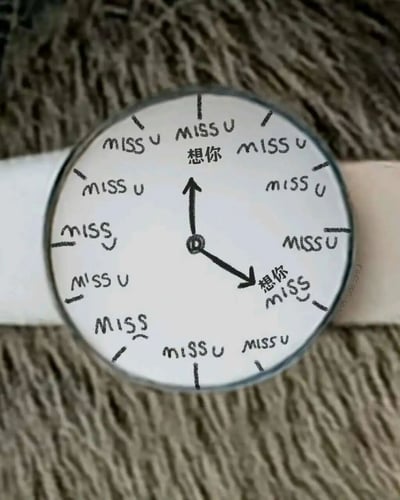 一张创意手表的照片，表盘上原本的数字被手写的"MISS U"和中文"想你"替代，时针和分针分别指向不同的"想你"字样，象征着每时每刻都在思念对方。手表为白色表带，放置在毛绒质地的棕色背景上，整体风格温馨浪漫。