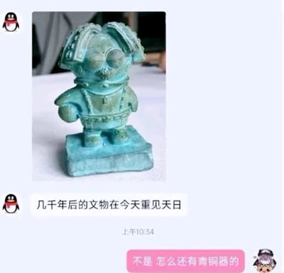 这是一张腾讯QQ的聊天界面截图，聊天中发送了一款创意文创摆件的照片：摆件将QQ企鹅的形象与三星堆青铜人像的标志性特征（夸张的眼部、独特的发型）相结合，表面做旧处理呈现出青铜器的铜绿色锈迹，整体造型酷似出土文物。发送者配文“几千年后的文物在今天重见天日”，以调侃的语气将这个现代文创比作未来出土的古代文物；接收者回复“不是 怎么还有青铜器的”，表达对这个混搭造型的惊讶与调侃，整体内容通过文创形象的跨界混搭，制造出幽默的玩梗效果。