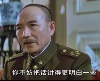 这是一张来自历史剧的截图，画面中一位身穿绿色军装的军事官员表情严肃地说着台词："你不妨把话讲得更明白一些"。背景中可以看到传统中式家具和装饰，营造出历史氛围。这句话常被网友在希望对方明确表达观点或解释清楚事情时使用，成为网络流行梗图。